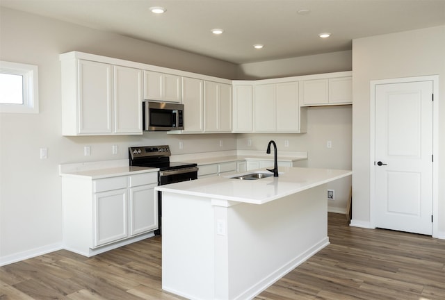 kitchen featuring appliances with stainless steel finishes, sink, hardwood / wood-style flooring, white cabinetry, and an island with sink