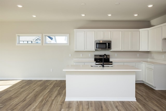 kitchen featuring light wood-type flooring, stainless steel appliances, white cabinetry, and an island with sink