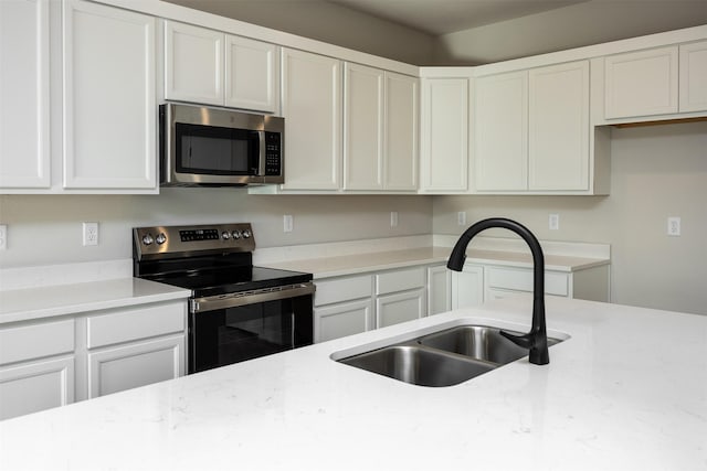 kitchen with appliances with stainless steel finishes, light stone counters, white cabinetry, and sink