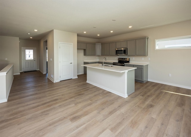 kitchen with light wood-type flooring, gray cabinetry, stainless steel appliances, a kitchen island with sink, and sink