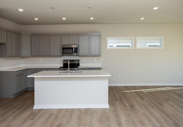 kitchen featuring stainless steel appliances, a kitchen island with sink, and gray cabinetry