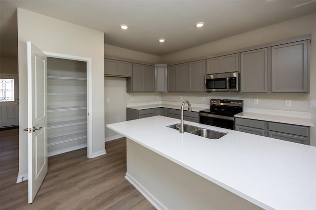 kitchen with sink, stainless steel appliances, wood-type flooring, gray cabinets, and a kitchen island with sink