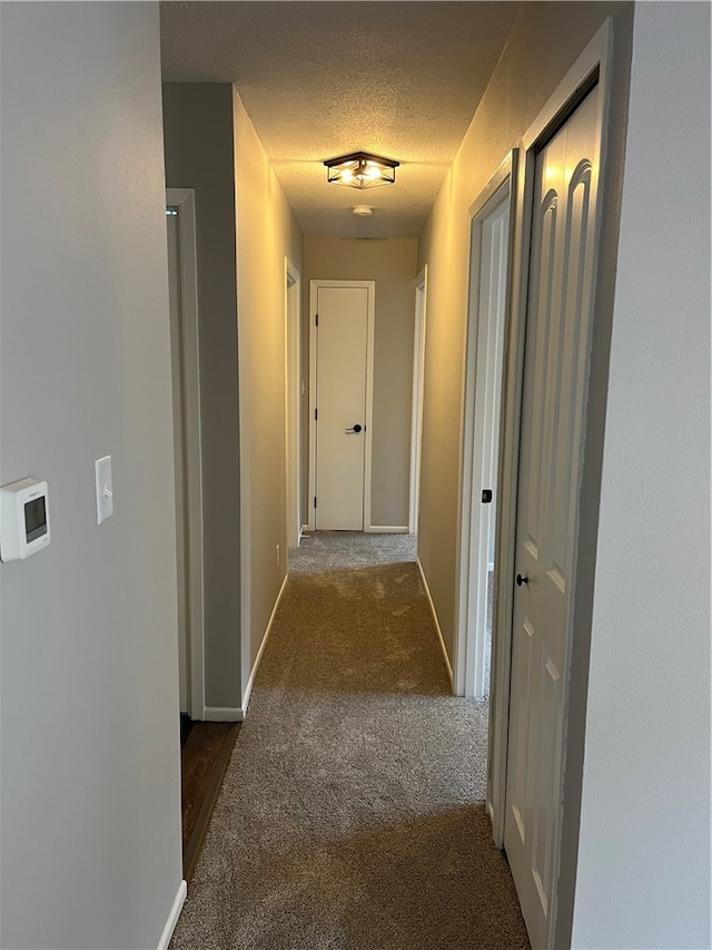 hallway with dark carpet and a textured ceiling