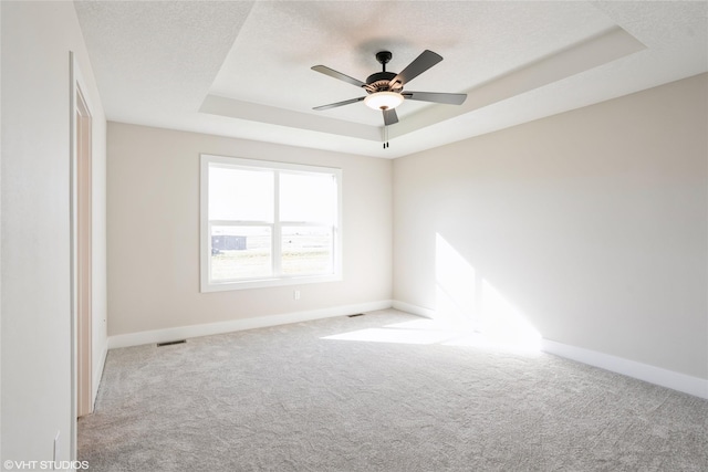 spare room featuring a tray ceiling, light carpet, and ceiling fan