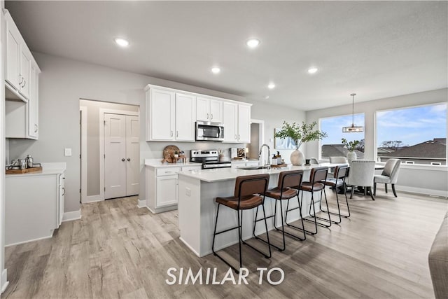 kitchen featuring white cabinetry, stainless steel appliances, light hardwood / wood-style floors, a center island with sink, and decorative light fixtures