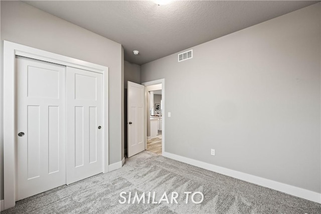 unfurnished bedroom featuring light carpet, a closet, and a textured ceiling