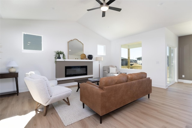 living area with lofted ceiling, light wood-type flooring, a glass covered fireplace, and baseboards