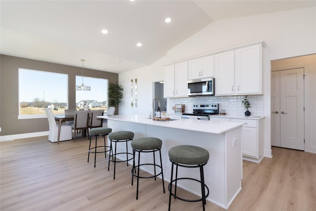 kitchen with stainless steel appliances, white cabinetry, backsplash, a kitchen bar, and a center island with sink