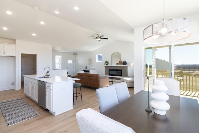 dining room with a glass covered fireplace, ceiling fan with notable chandelier, vaulted ceiling, light wood-type flooring, and recessed lighting