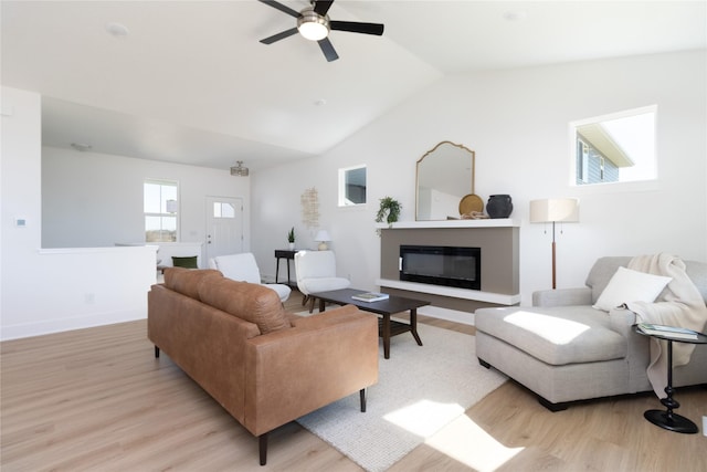 living room featuring light wood-style floors, a glass covered fireplace, vaulted ceiling, ceiling fan, and baseboards