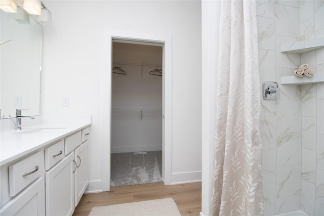 full bath with wood finished floors, vanity, baseboards, a tile shower, and a walk in closet