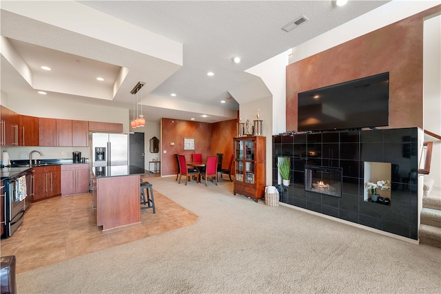 kitchen with a center island, hanging light fixtures, appliances with stainless steel finishes, light colored carpet, and a breakfast bar area