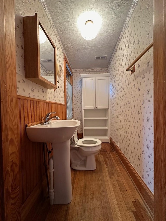 bathroom with a textured ceiling, toilet, crown molding, and hardwood / wood-style flooring