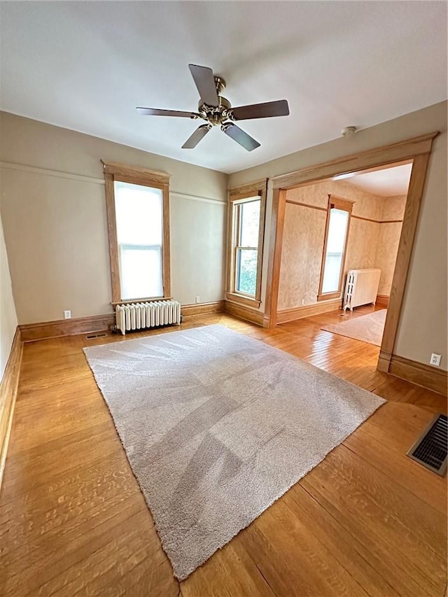 unfurnished room with ceiling fan, radiator, and light hardwood / wood-style flooring