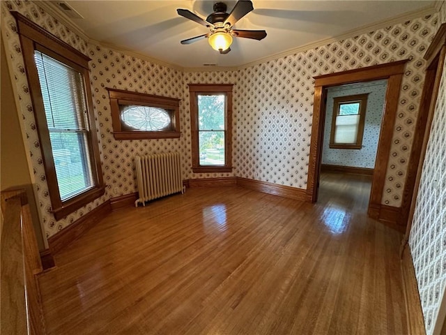 empty room with crown molding, wood-type flooring, radiator heating unit, and ceiling fan