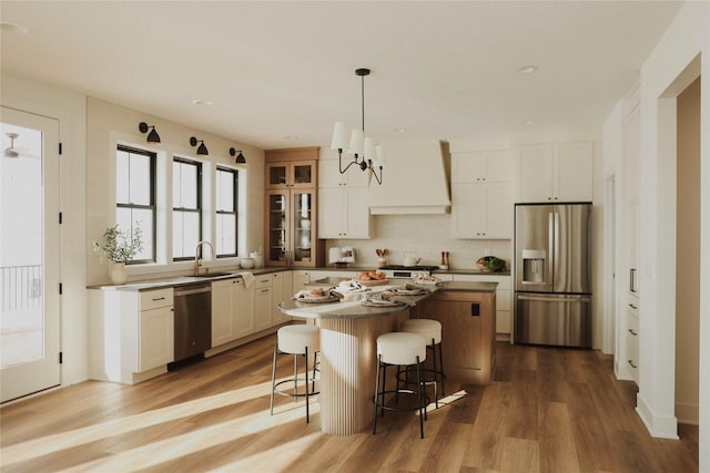 kitchen featuring appliances with stainless steel finishes, premium range hood, white cabinets, a center island, and hanging light fixtures