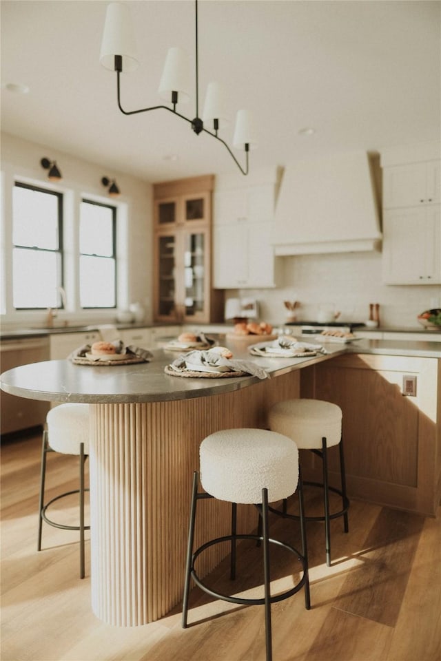 kitchen featuring premium range hood, a breakfast bar, light hardwood / wood-style flooring, a center island, and white cabinetry