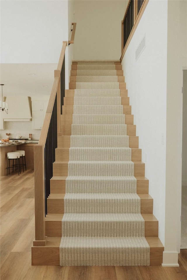 stairway with hardwood / wood-style floors and an inviting chandelier