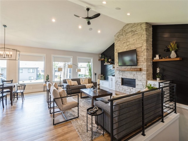 living room with light wood-type flooring, ceiling fan with notable chandelier, a fireplace, and vaulted ceiling