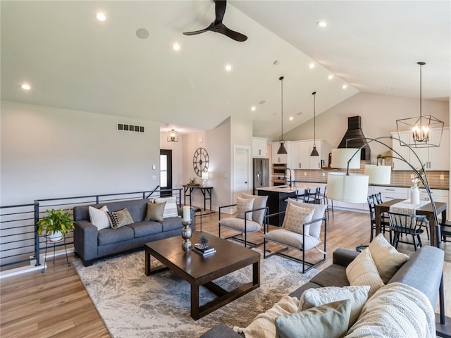 living room with ceiling fan with notable chandelier, vaulted ceiling, and light hardwood / wood-style floors