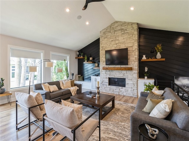 living room with ceiling fan, a stone fireplace, light hardwood / wood-style flooring, and vaulted ceiling