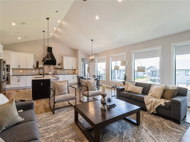 living room with lofted ceiling, light wood-type flooring, sink, and a chandelier