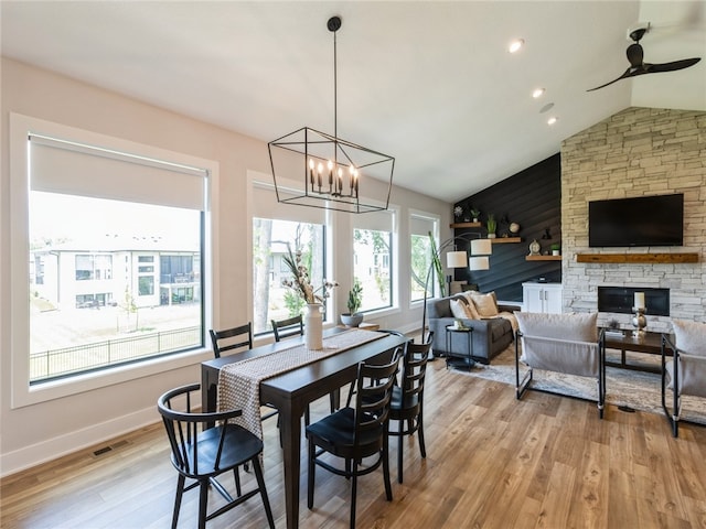 dining area with ceiling fan with notable chandelier, light wood-type flooring, lofted ceiling, and a fireplace