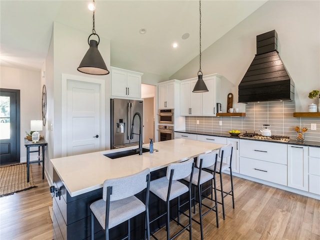 kitchen with stainless steel appliances, decorative light fixtures, custom range hood, and a center island with sink