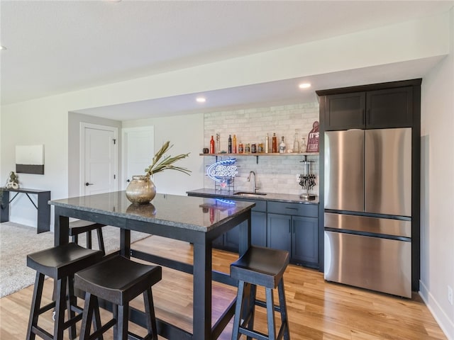 bar featuring stainless steel fridge, sink, dark stone counters, light hardwood / wood-style floors, and decorative backsplash