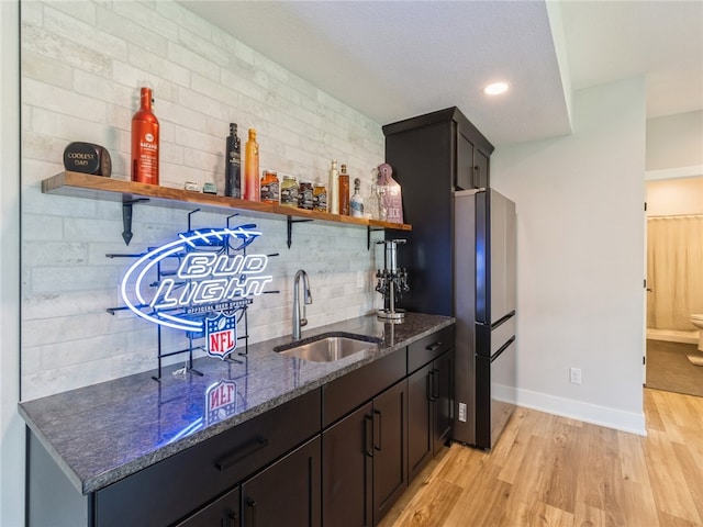 kitchen with sink, light hardwood / wood-style flooring, backsplash, stainless steel refrigerator, and dark stone counters