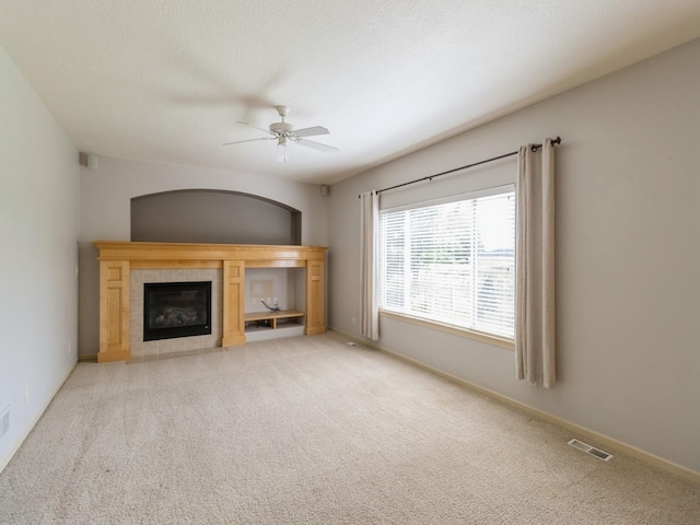 unfurnished living room with a tile fireplace, light carpet, visible vents, baseboards, and a ceiling fan