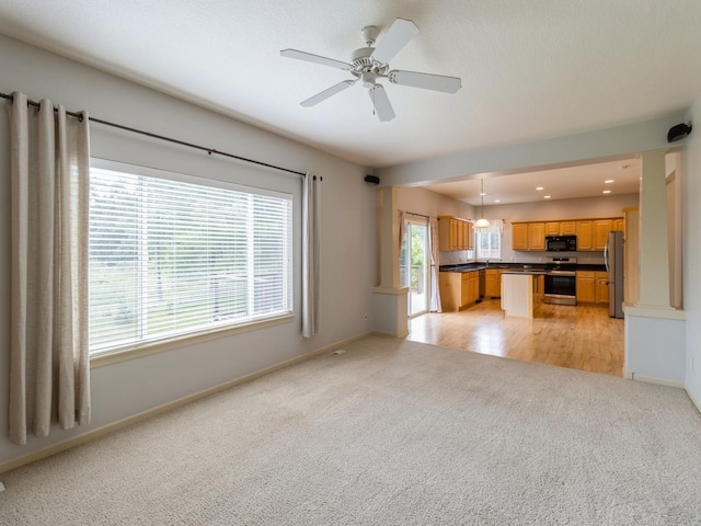 unfurnished living room featuring baseboards, a ceiling fan, and light colored carpet