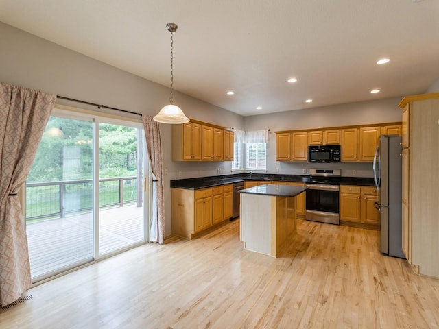 kitchen with light wood-style flooring, hanging light fixtures, appliances with stainless steel finishes, a center island, and dark countertops