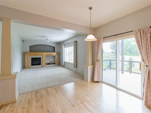 unfurnished living room with ornate columns, a fireplace, light wood-style flooring, and baseboards