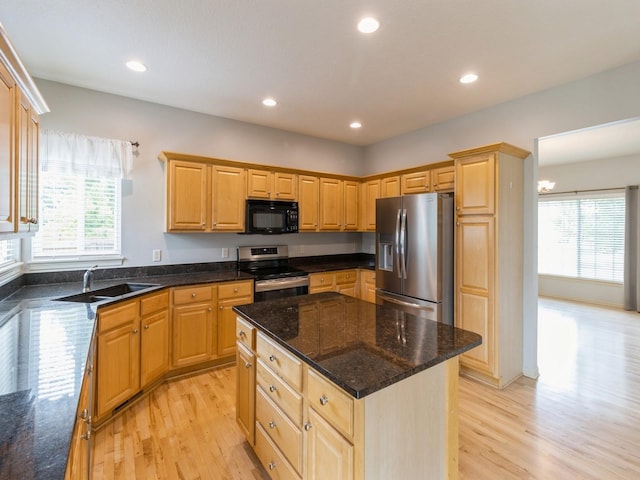 kitchen with a sink, appliances with stainless steel finishes, dark stone counters, and a kitchen island