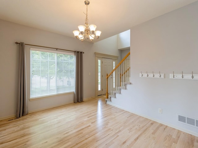 spare room with a chandelier, light wood-type flooring, visible vents, and stairway