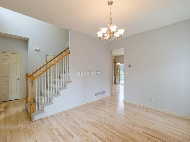 unfurnished room featuring light wood-type flooring, visible vents, stairway, and an inviting chandelier