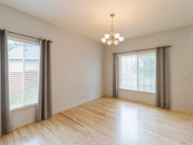 empty room with light wood-type flooring, a wealth of natural light, a notable chandelier, and baseboards