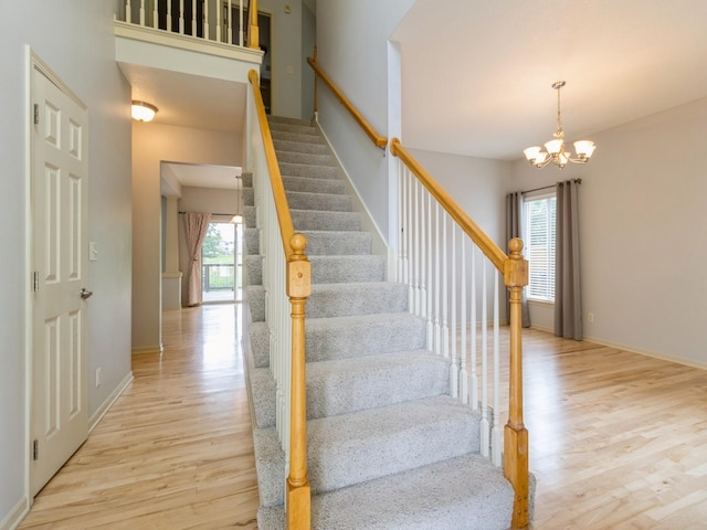 staircase with a chandelier, a wealth of natural light, baseboards, and wood finished floors