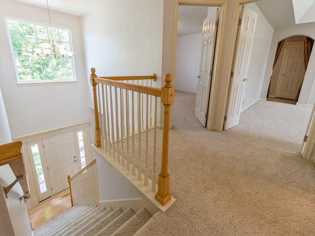 hall with a chandelier, arched walkways, an upstairs landing, and light colored carpet