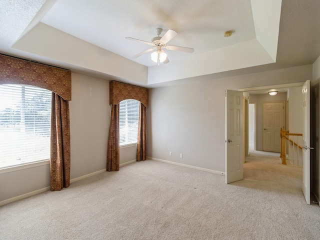 empty room featuring a tray ceiling, light colored carpet, and baseboards