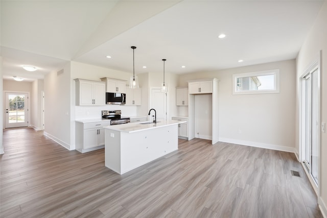 kitchen with pendant lighting, an island with sink, sink, white cabinetry, and appliances with stainless steel finishes