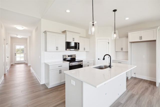 kitchen featuring sink, white cabinetry, a center island with sink, appliances with stainless steel finishes, and decorative light fixtures