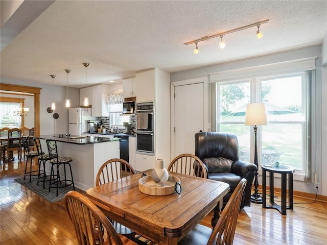 dining area with rail lighting, a textured ceiling, and light wood-type flooring