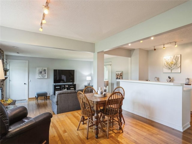 dining area featuring a stone fireplace, a textured ceiling, and light hardwood / wood-style flooring