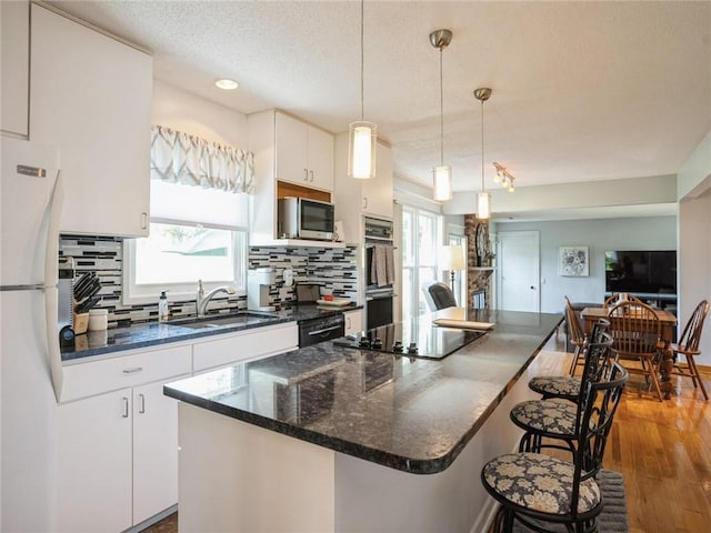 kitchen featuring decorative backsplash, a kitchen island, black appliances, white cabinets, and sink