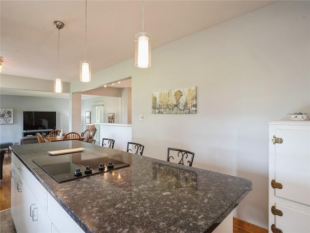 kitchen with white cabinetry, black electric cooktop, a kitchen breakfast bar, hanging light fixtures, and a center island