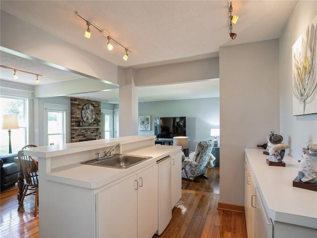 kitchen with wood-type flooring, sink, white cabinetry, a kitchen island with sink, and a textured ceiling