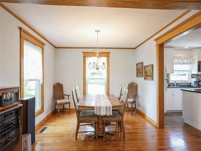 dining space with light hardwood / wood-style floors, plenty of natural light, a textured ceiling, and a notable chandelier