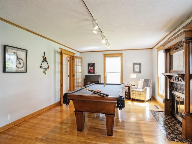 playroom featuring rail lighting, pool table, a textured ceiling, ornamental molding, and light hardwood / wood-style flooring